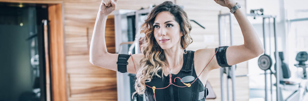 EMS electro stimulation women exercises with coach in modern gym. Electric muscle stimulation workout